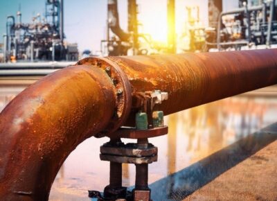 Corroded industrial pipe with rust damage in a refinery setting.