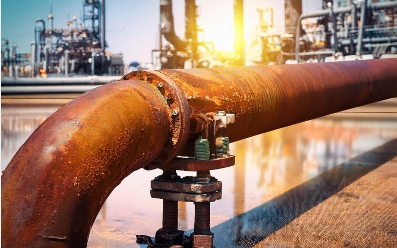 Corroded industrial pipe with rust damage in a refinery setting.