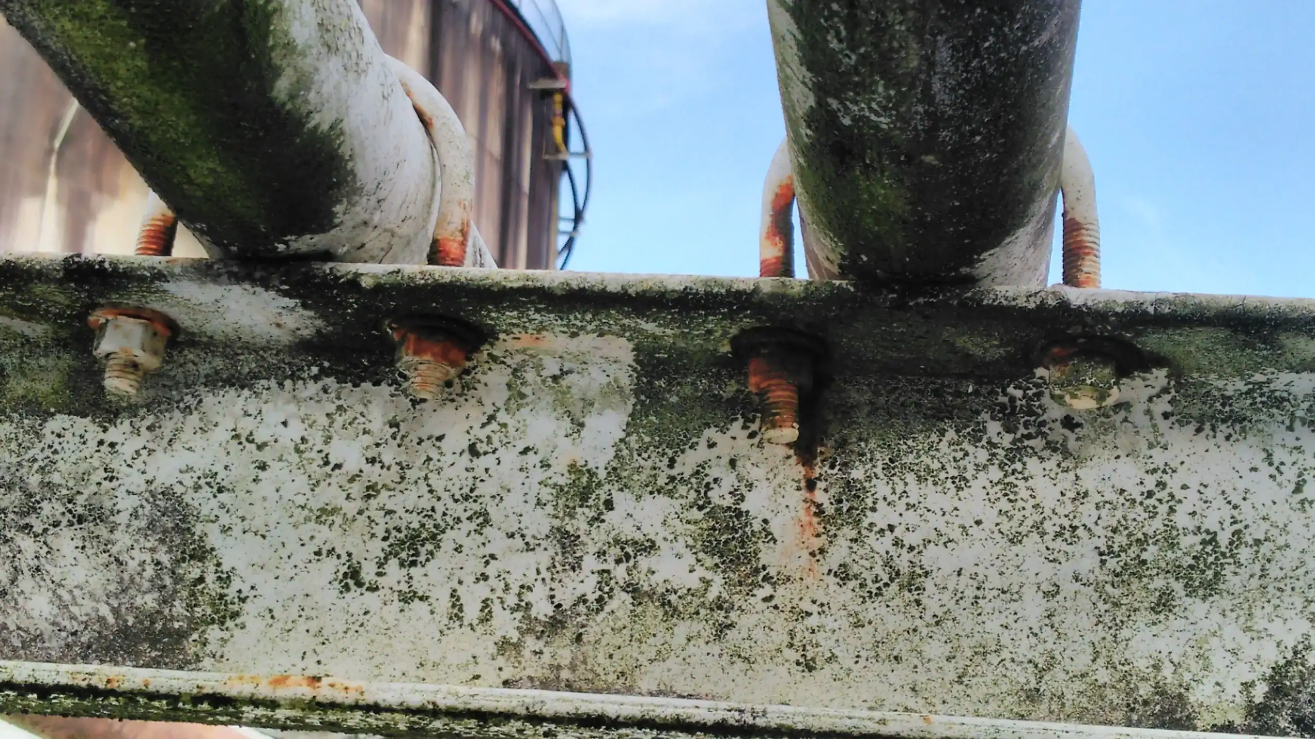 Corroded welded pipe support showing rust and moisture damage under U-bolts