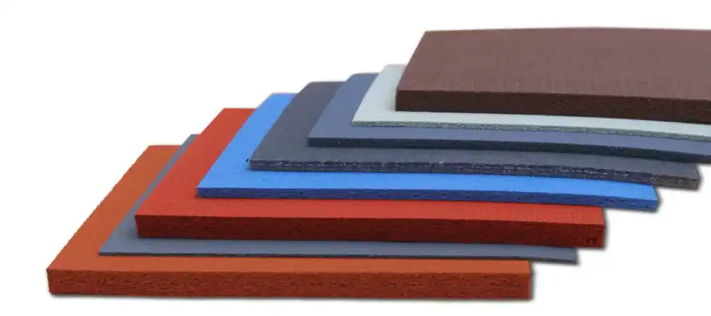 Stacked sheets of industrial gasket and isolation liner materials in different colors, thicknesses, and textures for pipe support applications.